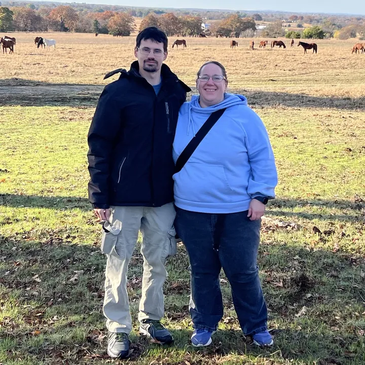 Keith and Emily in a field with horses grazing behind them
